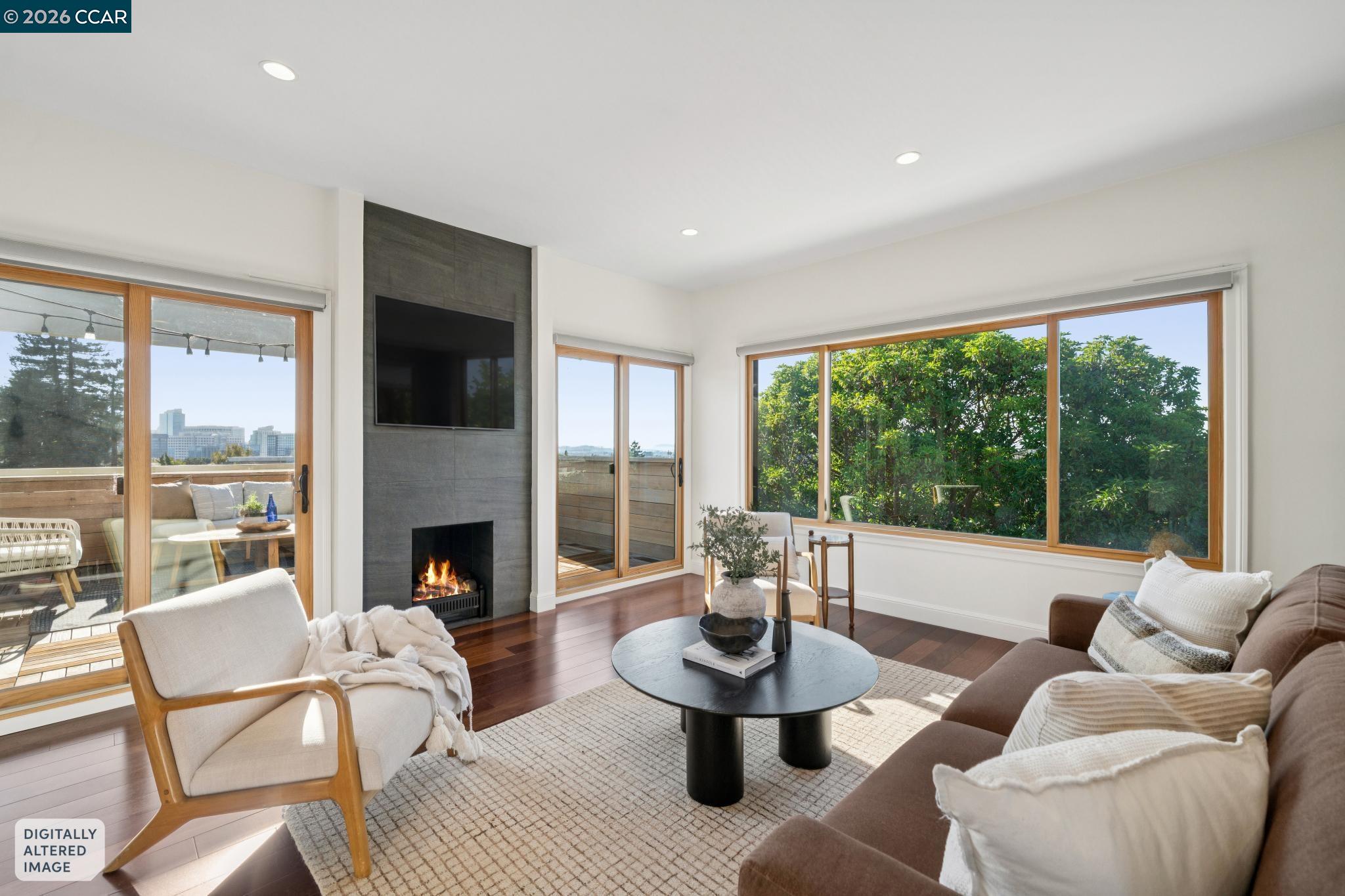 Living room with a tiled fireplace, large windows, hardwood floors, and sliding doors to a furnished deck.