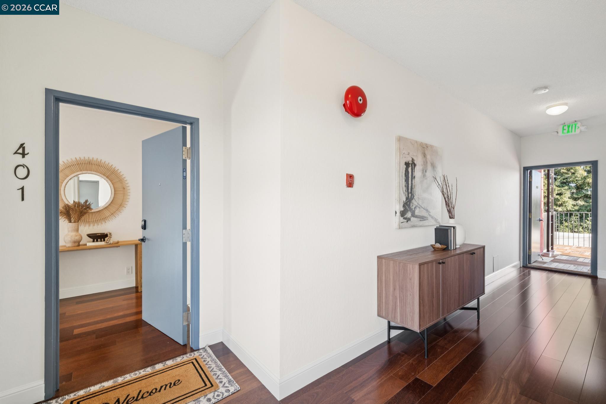 Condominium entry foyer with dark wood floors, a blue-gray door, and an open doorway to the balcony.