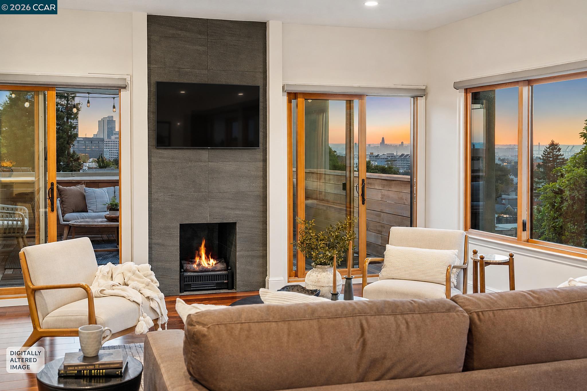 Living room with a stone fireplace and wide windows overlooking the city and water at sunset.