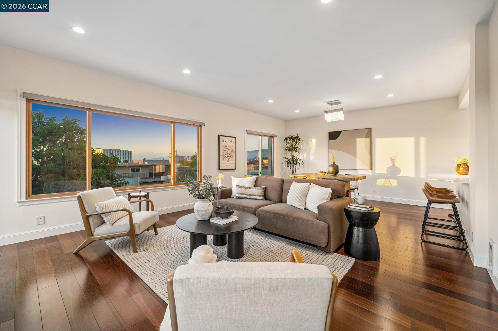 Living room with a brown sofa, dark hardwood floors, and large windows overlooking nearby buildings.