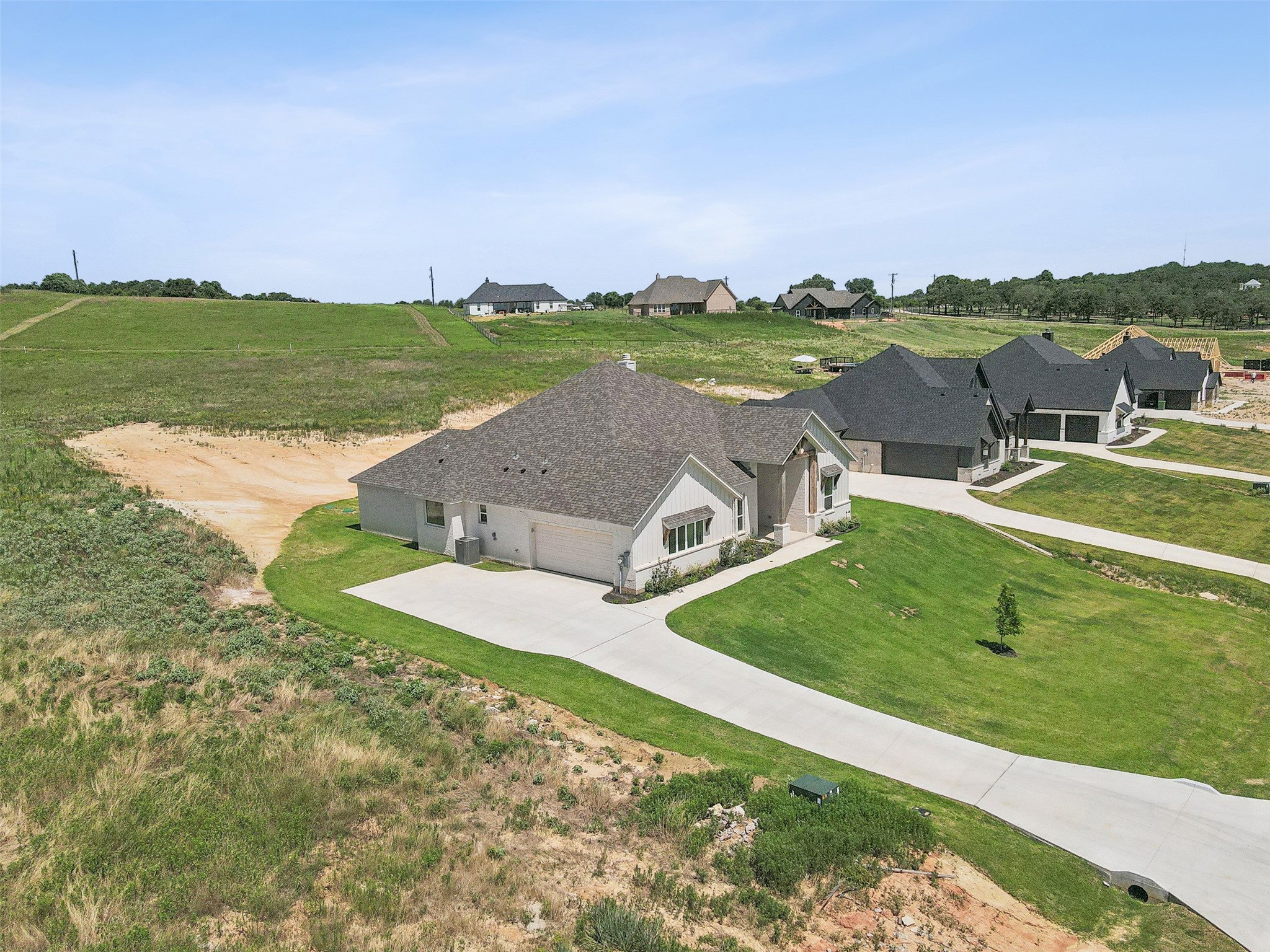 Aerial view of a single-story home with a curved driveway beside open land and neighboring houses.