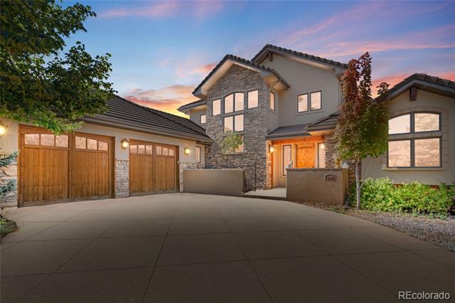 Two-story stone-and-stucco home with wood garage doors and a wide driveway at dusk.