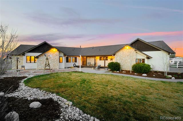 Single-story stone-accented home at dusk, with a curved lawn and illuminated covered patio.