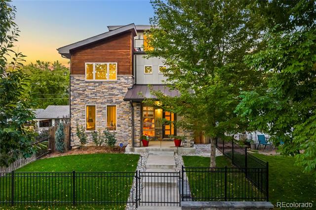 Two-story home with a stone facade, landscaped lawn, and fenced front yard at dusk.