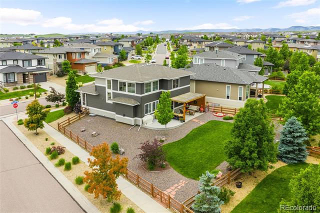 Modern gray home with a fenced gravel yard and covered patio, surrounded by neighborhood homes.