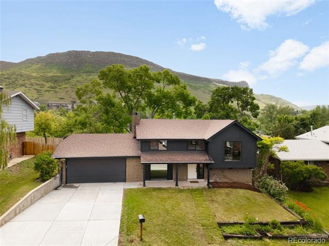 Dark gray two-story home with an attached garage, backed by green foothills and a mountain.