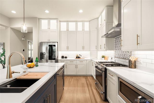 Bright white kitchen with a large island, black sink, stainless steel appliances, and light wood floors.