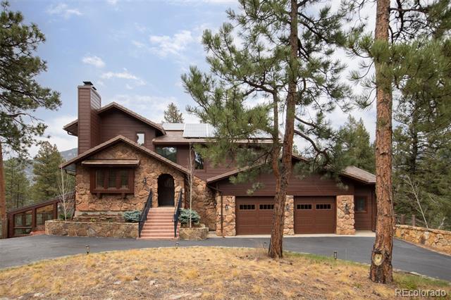 Mountain home with stone-and-wood exterior, two garage doors, and pine trees in front.