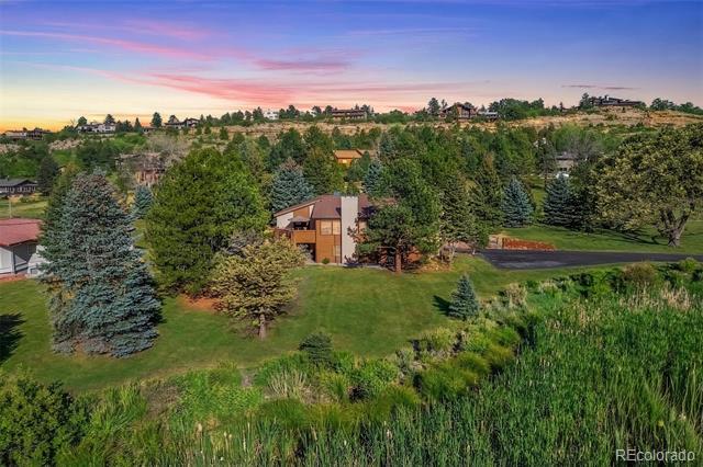 Elevated view of a home amid mature trees, lawn, and surrounding foothills at sunset.