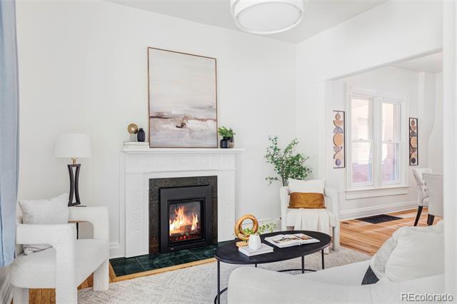 Living room with a lit fireplace, white seating, and an adjoining dining area with wood floors.