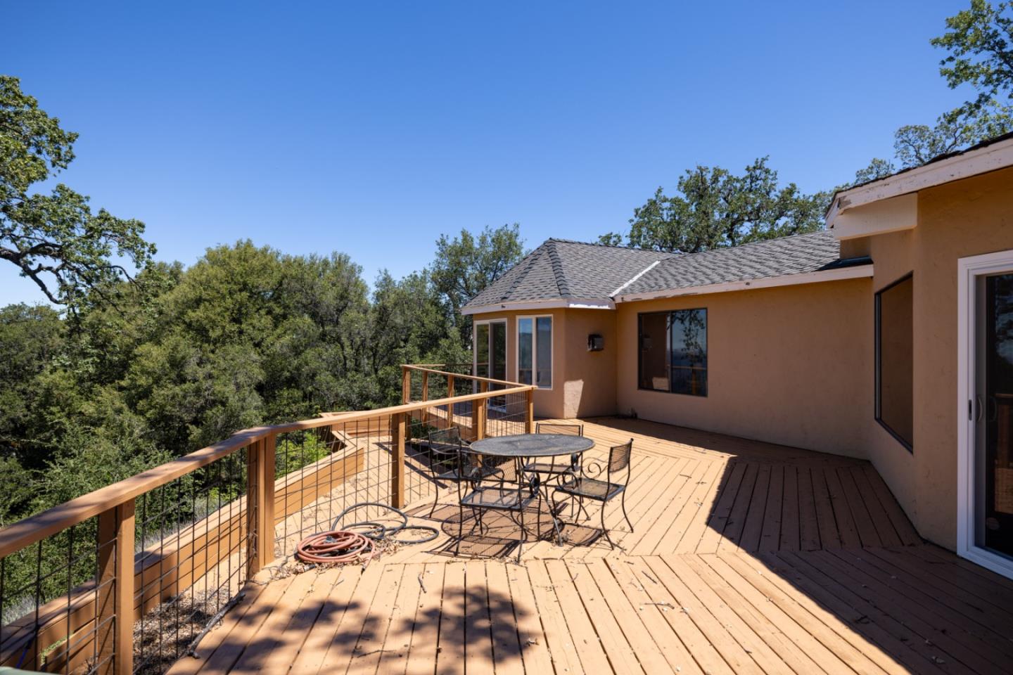 Spacious wooden deck with patio table and chairs, overlooking leafy trees