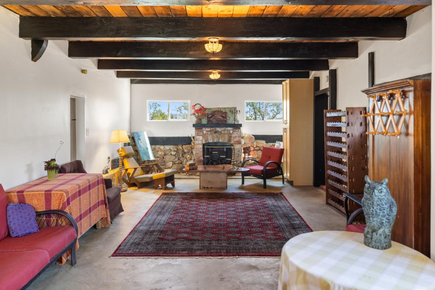 Living room with exposed beams, a stone fireplace, colorful seating, and a patterned rug.