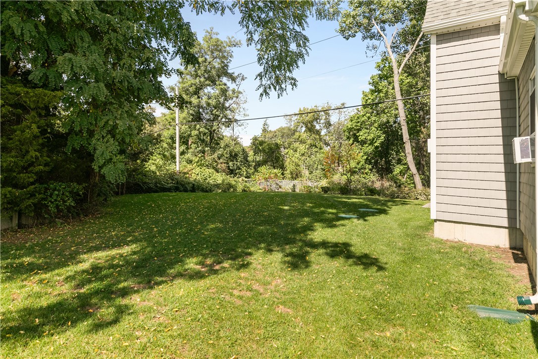 Side yard with a broad lawn, mature trees, and gray-shingled house.