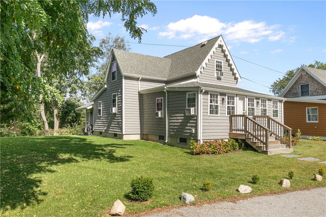 Gray shingle-sided house with multiple gables, a raised wooden deck, and a broad lawn.
