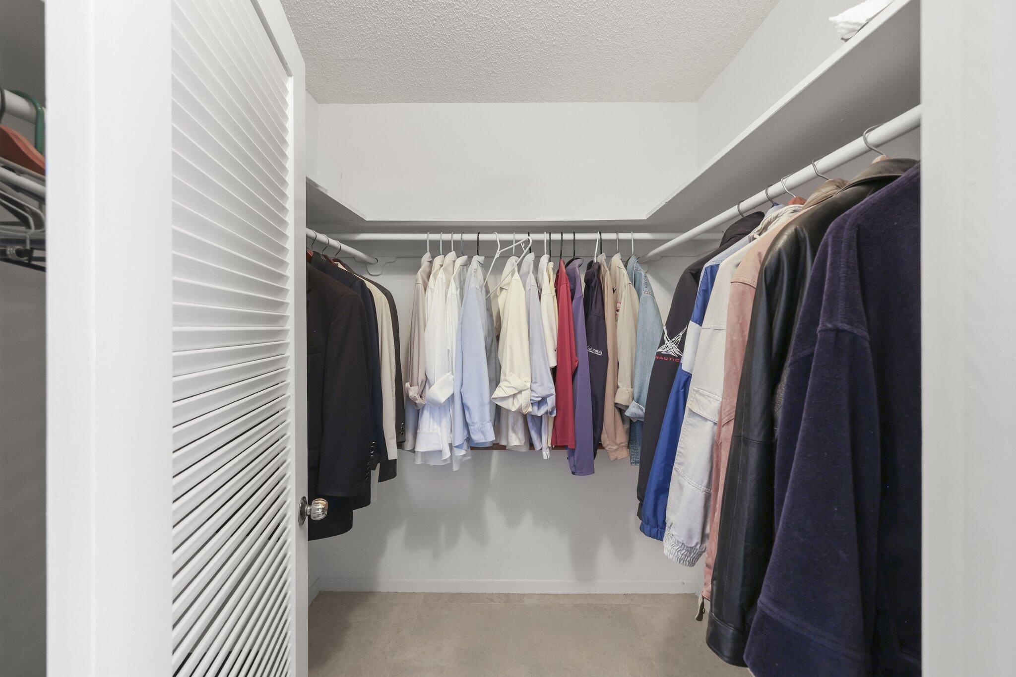 Walk-in closet with clothes on three sides and a white louvered door.