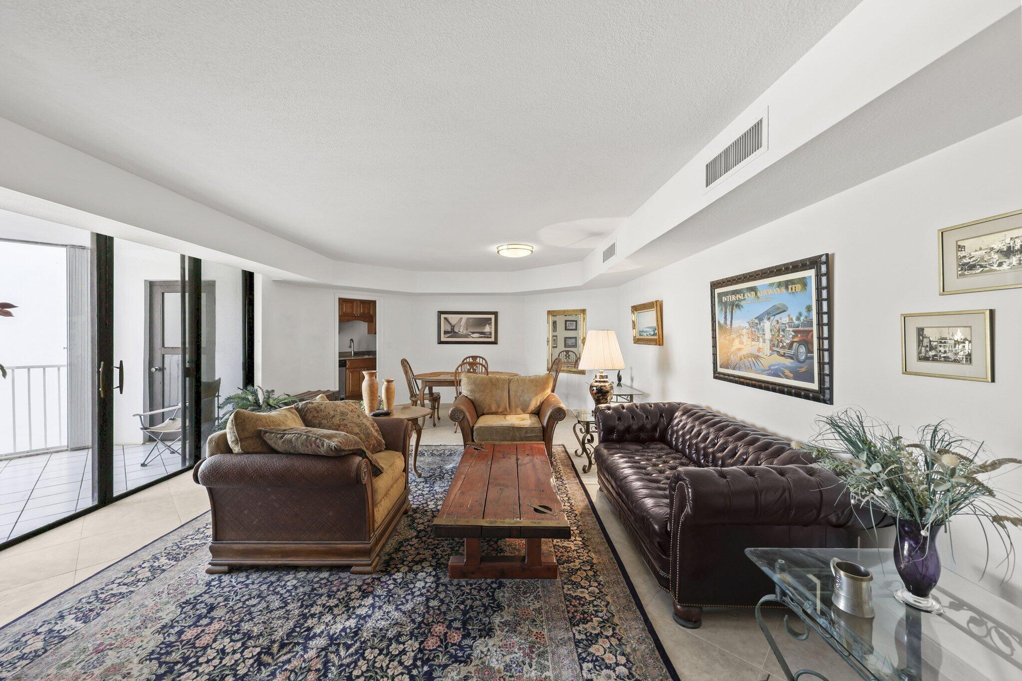 Living room with dark leather sofa, rustic coffee table, patterned rug, and sliding doors to a balcony.