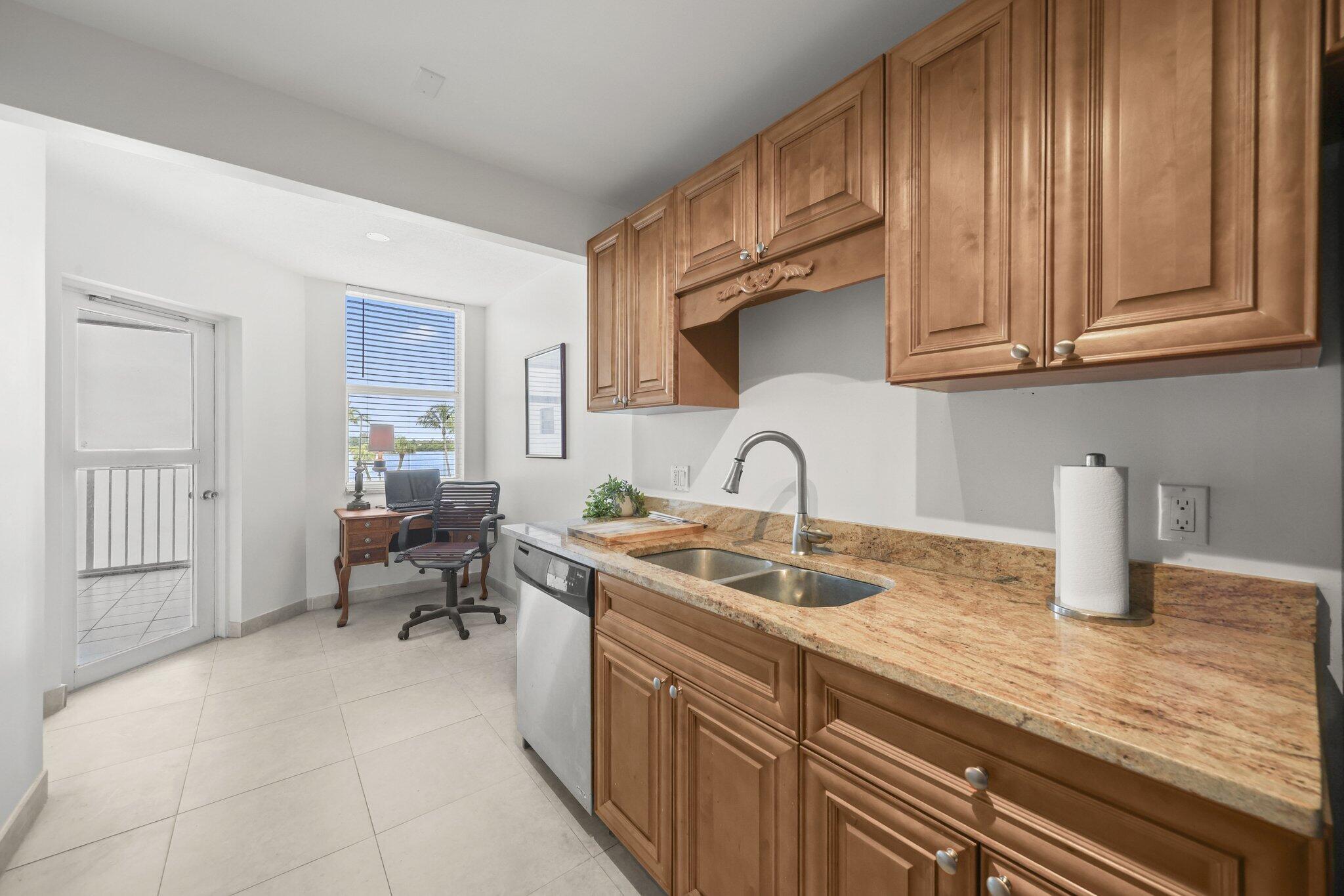 Condo kitchen with wood cabinets and granite counters, with palm trees and water visible through the window.