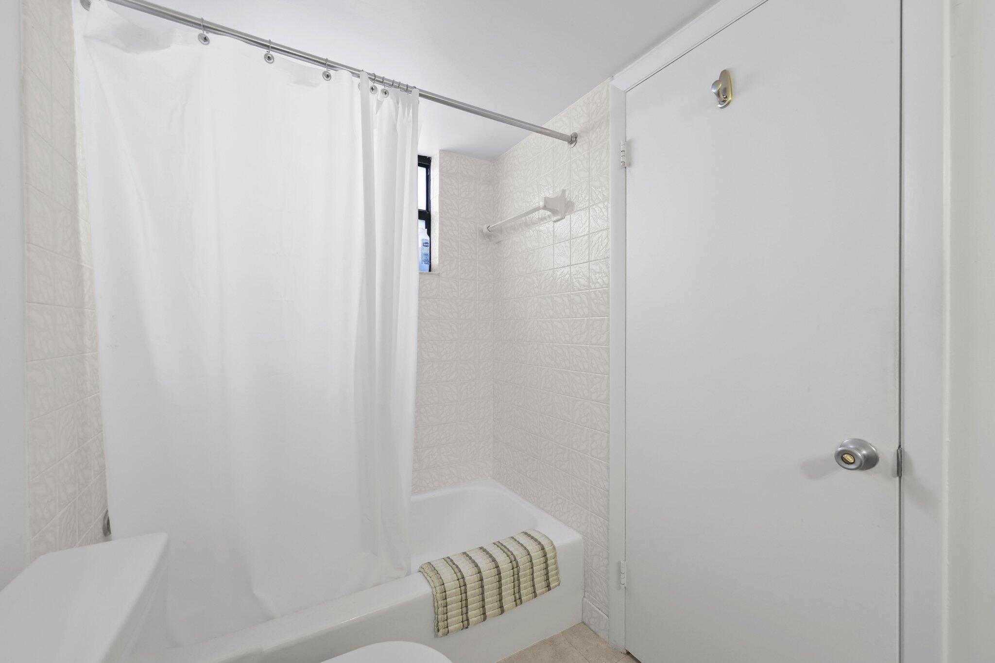 Bathroom with a white tub, shower curtain, textured tile, and striped towel.