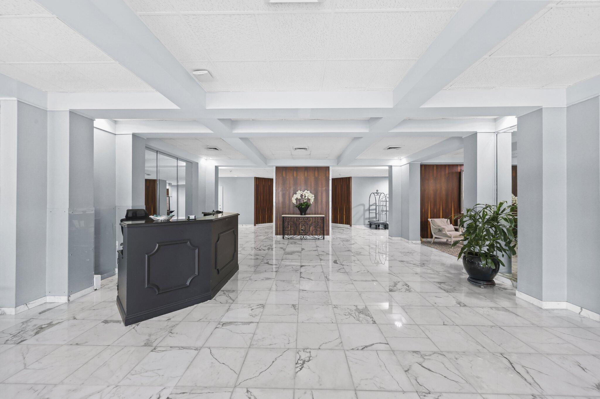 Condominium lobby with a dark reception desk, marble flooring, wood accents, and potted plants.