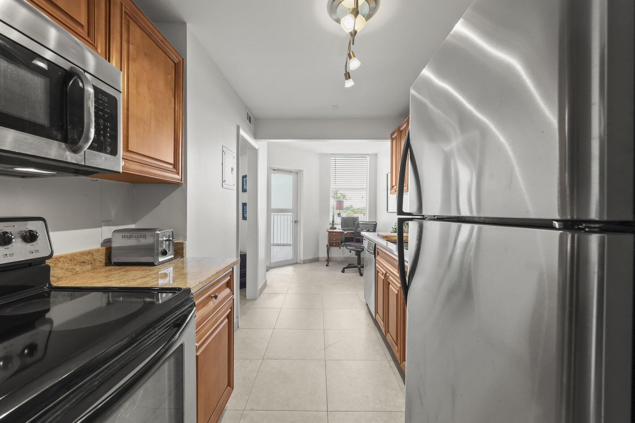 Kitchen with warm wood cabinets, granite counters, and stainless steel refrigerator.