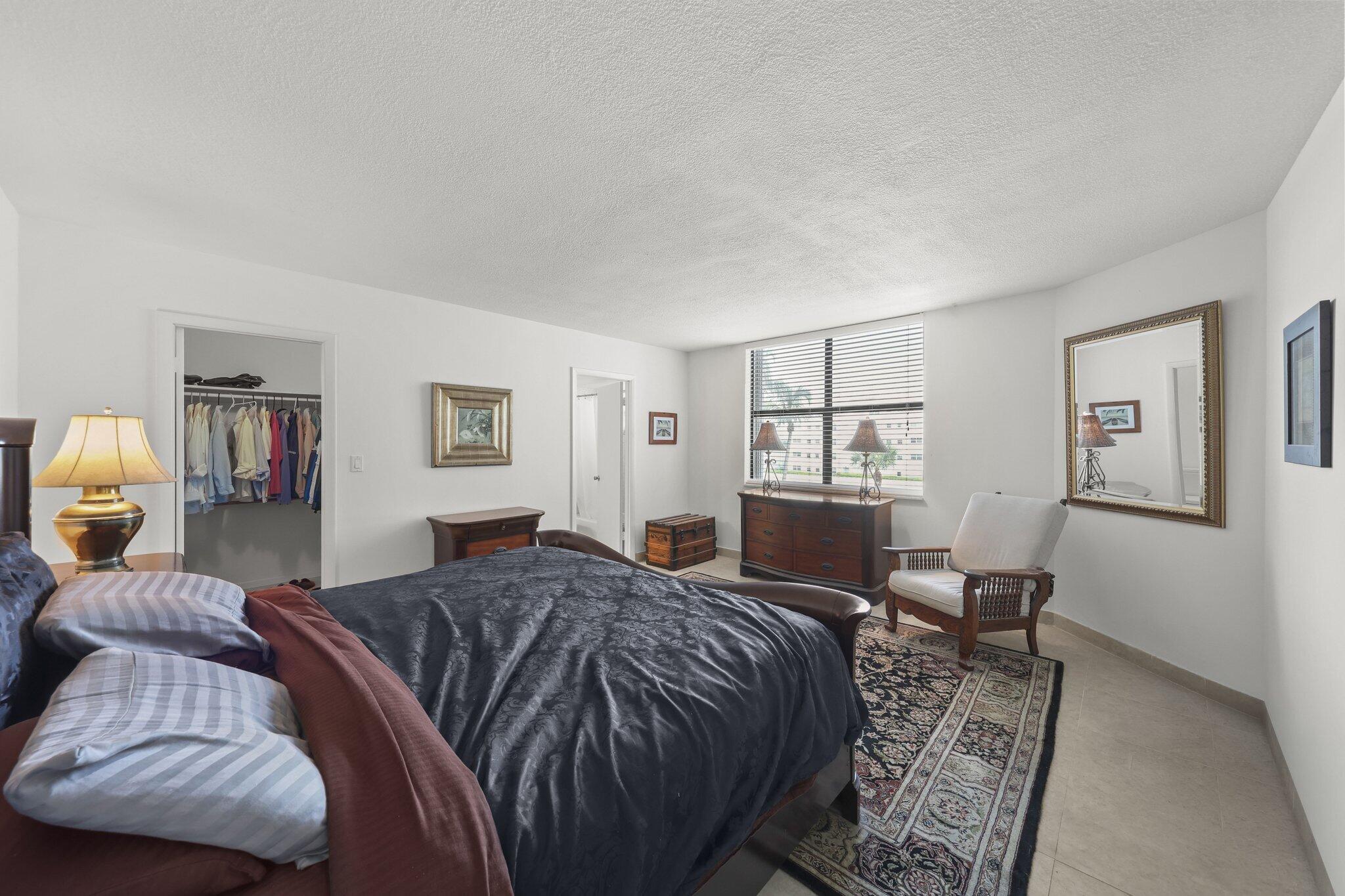 Furnished bedroom with a dark bedspread, walk-in closet, and large window with blinds.