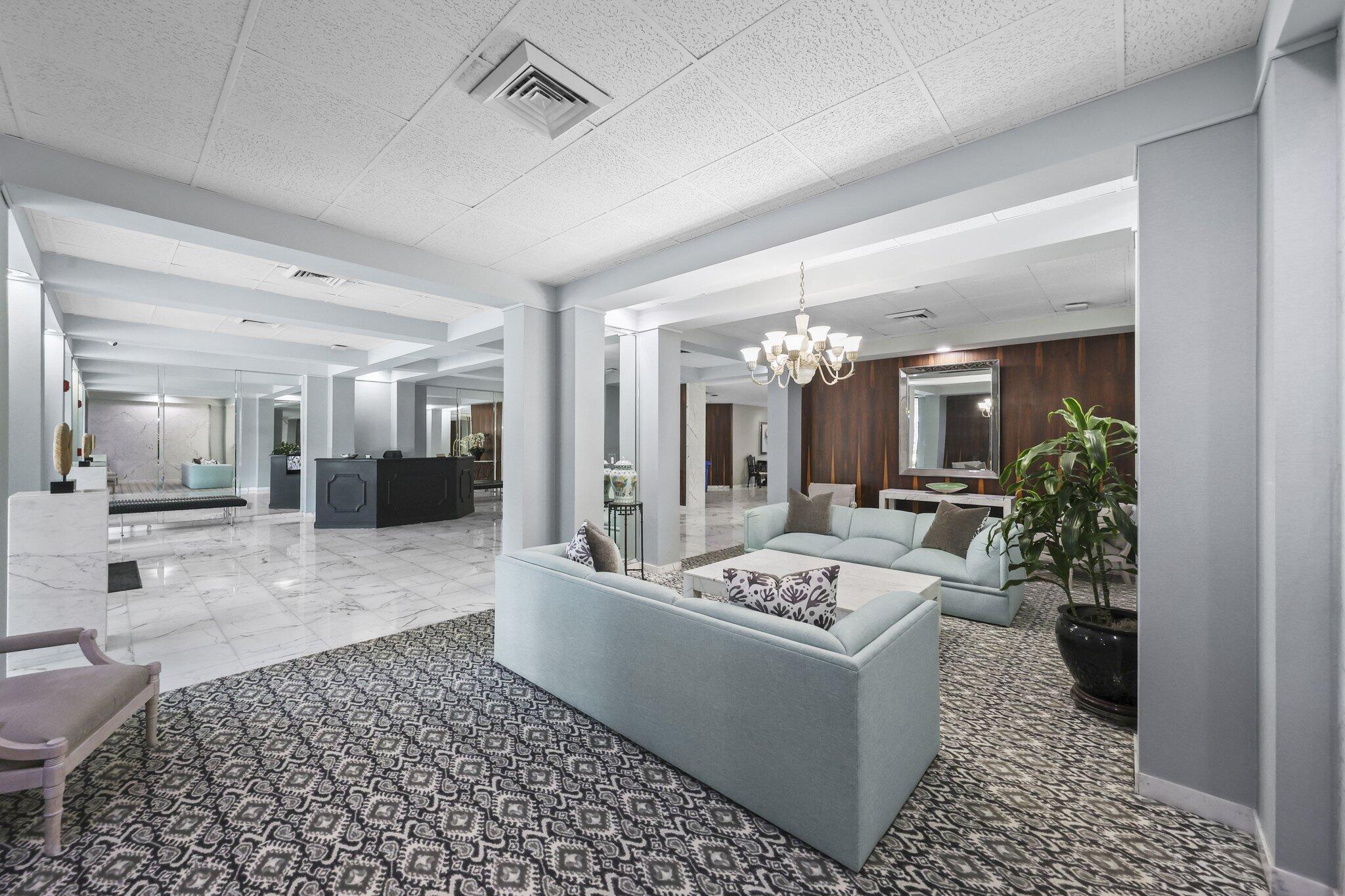 Condominium lobby with pale blue sofas, patterned rugs, and a chandelier.