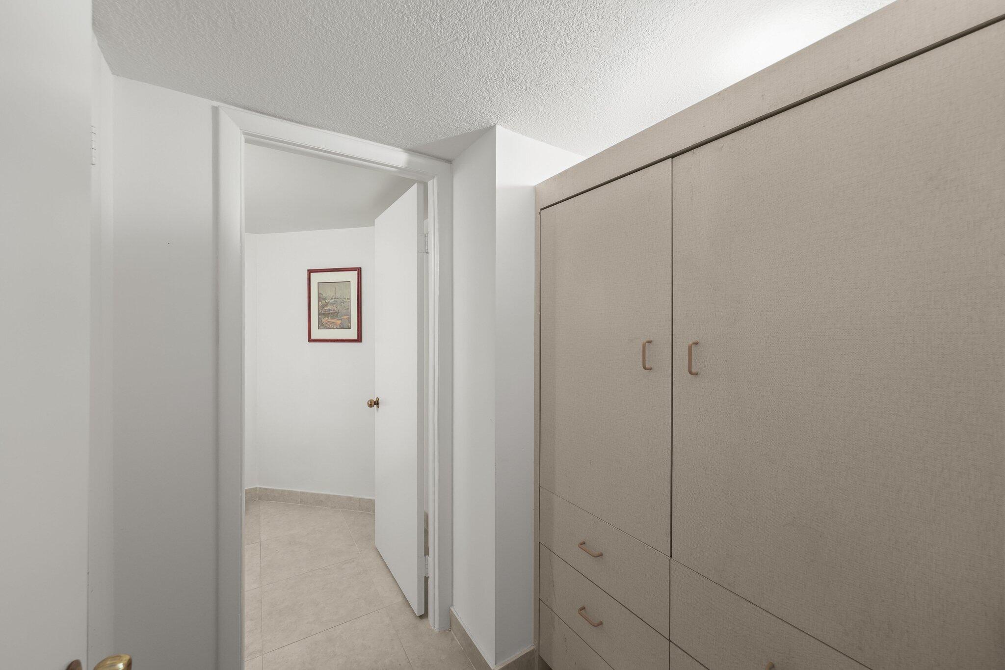 Tiled passage with built-in beige cabinets and an open doorway to a framed picture.