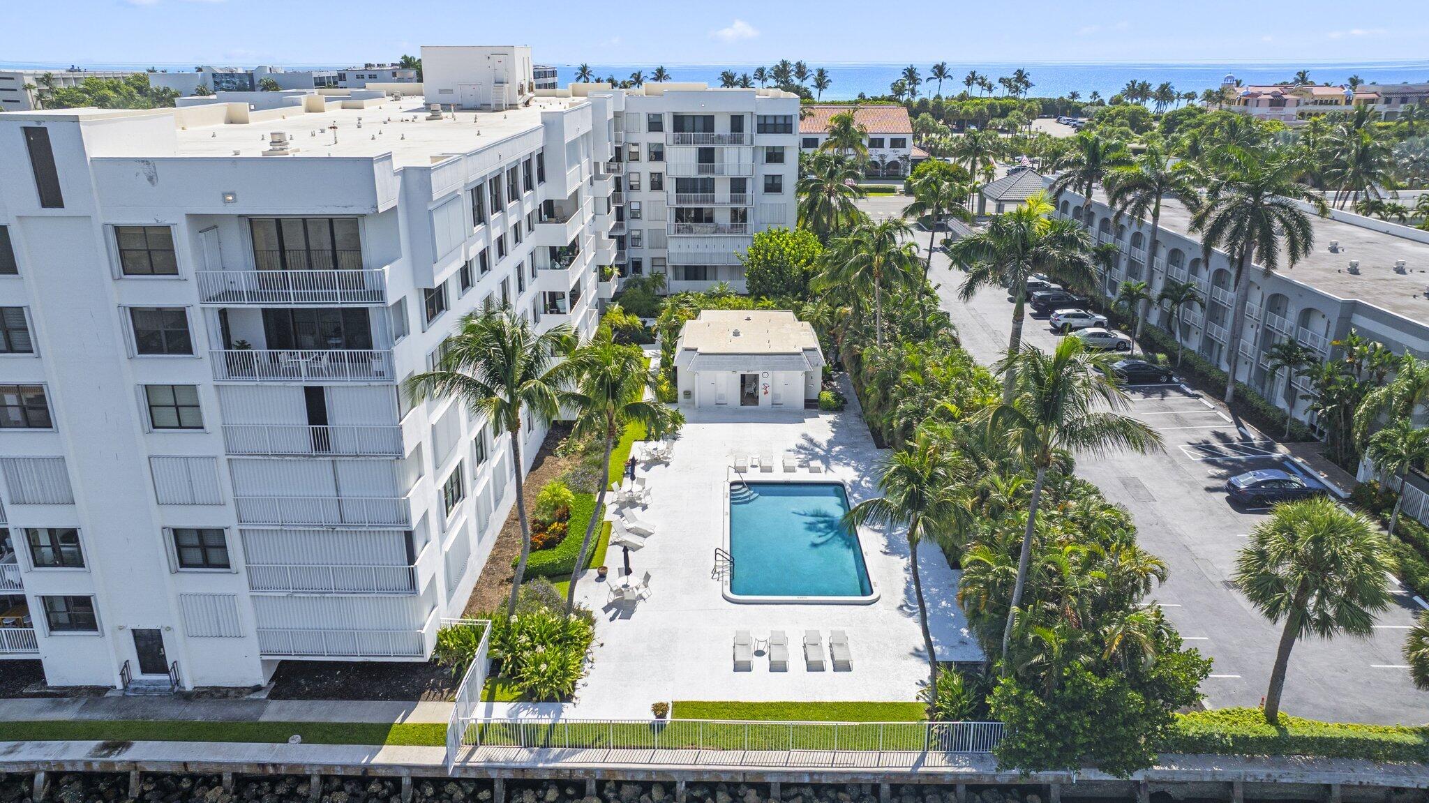 Aerial view of a beachfront condominium complex with a central pool and ocean beyond.