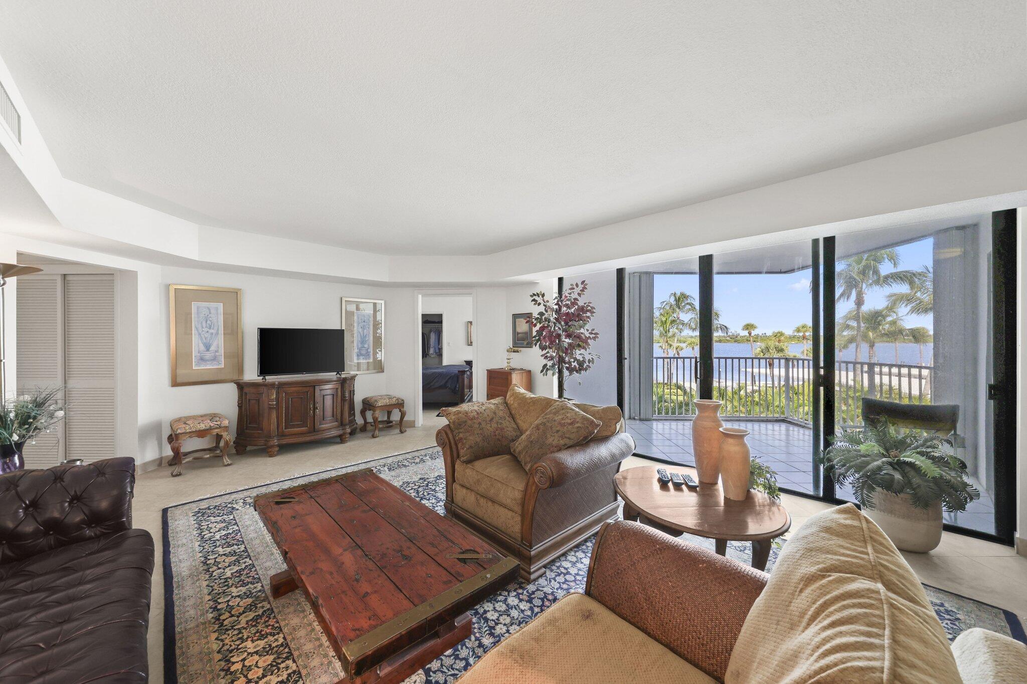 Furnished living room with traditional seating and a balcony overlooking palm trees and water.