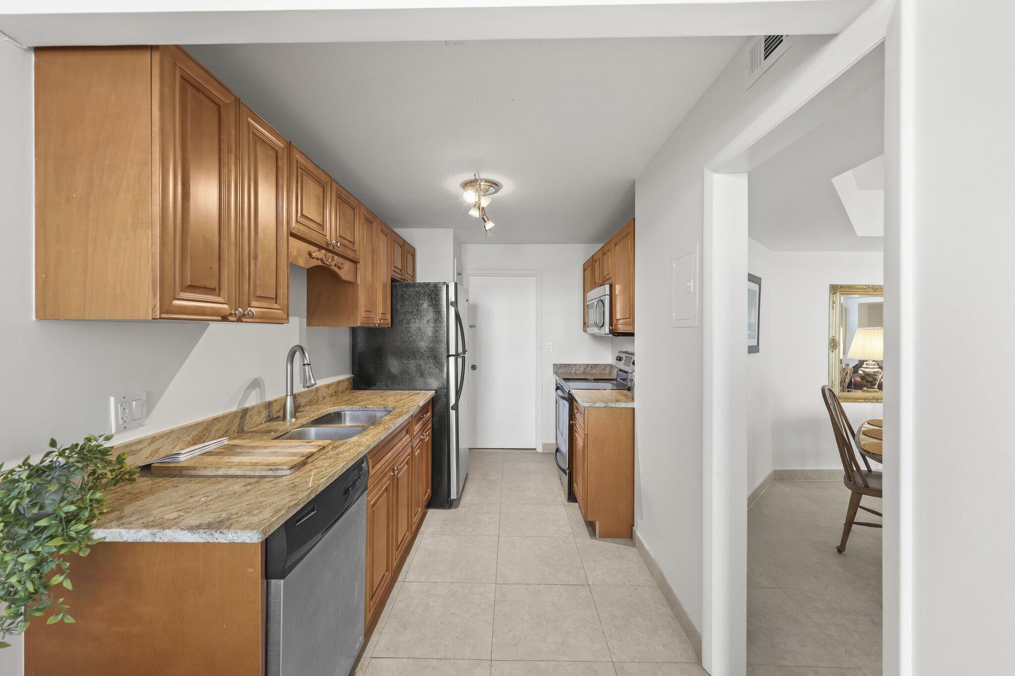 Galley kitchen with wood cabinets, granite counters, and stainless steel appliances beside the dining area.