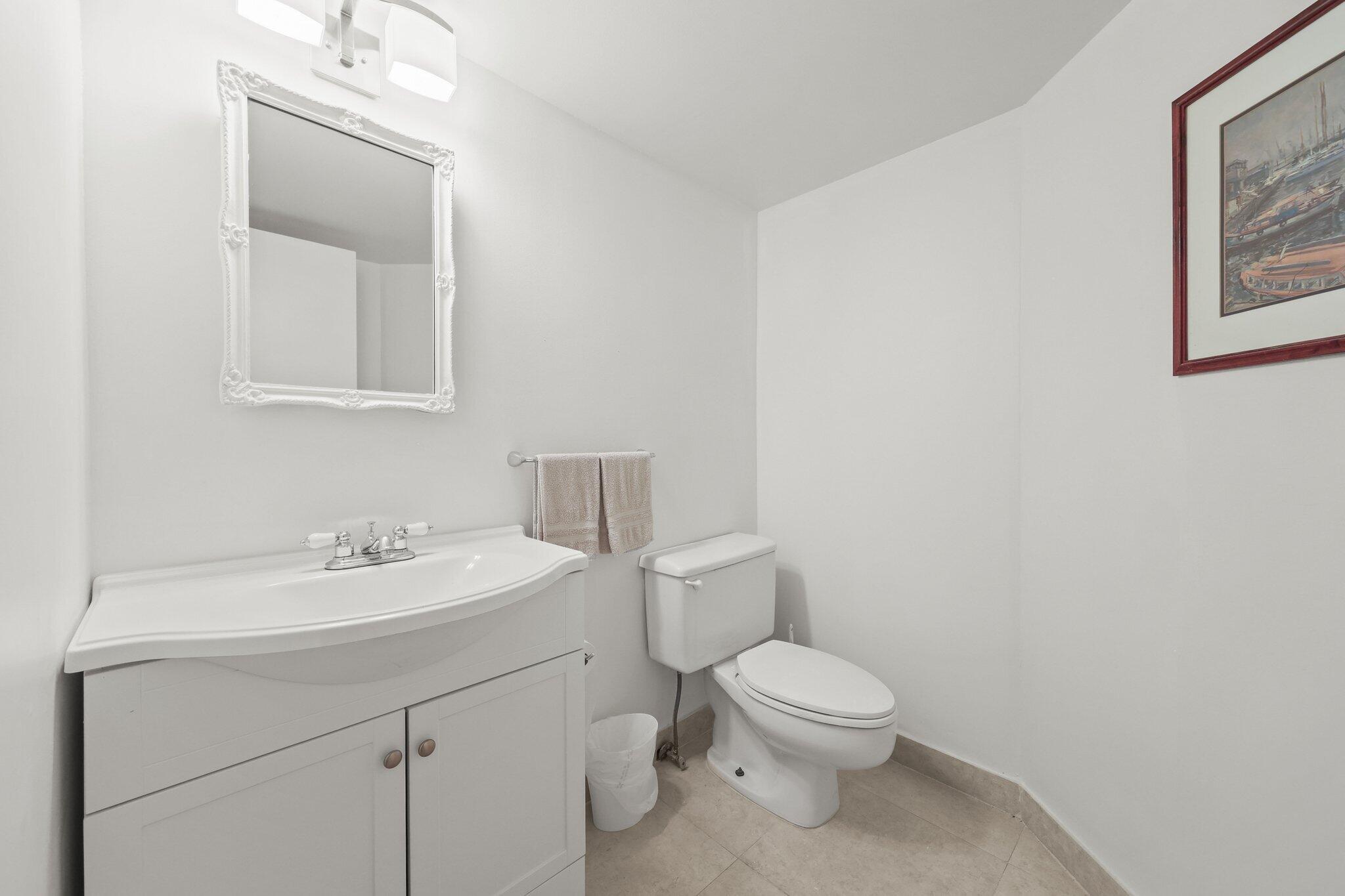 White bathroom with a vanity, ornate mirror, toilet, and beige tile floor.