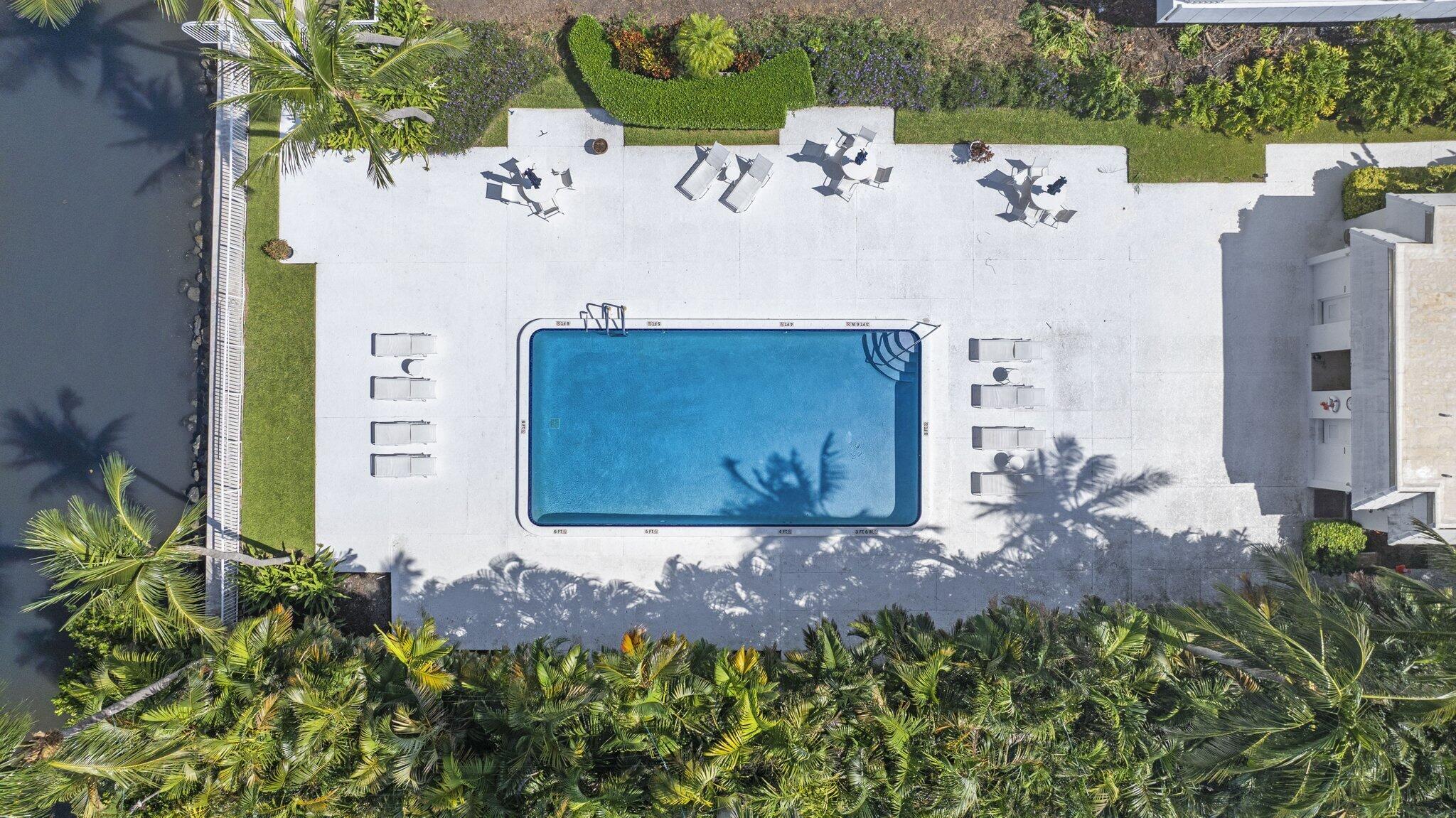 Aerial view of a swimming pool and surrounding deck, lounge chairs, and tropical landscaping.