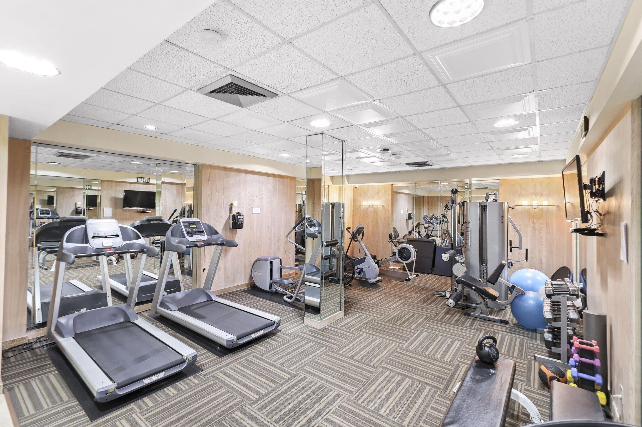 Fitness room with mirrored walls, treadmills, weight machines, and free weights.