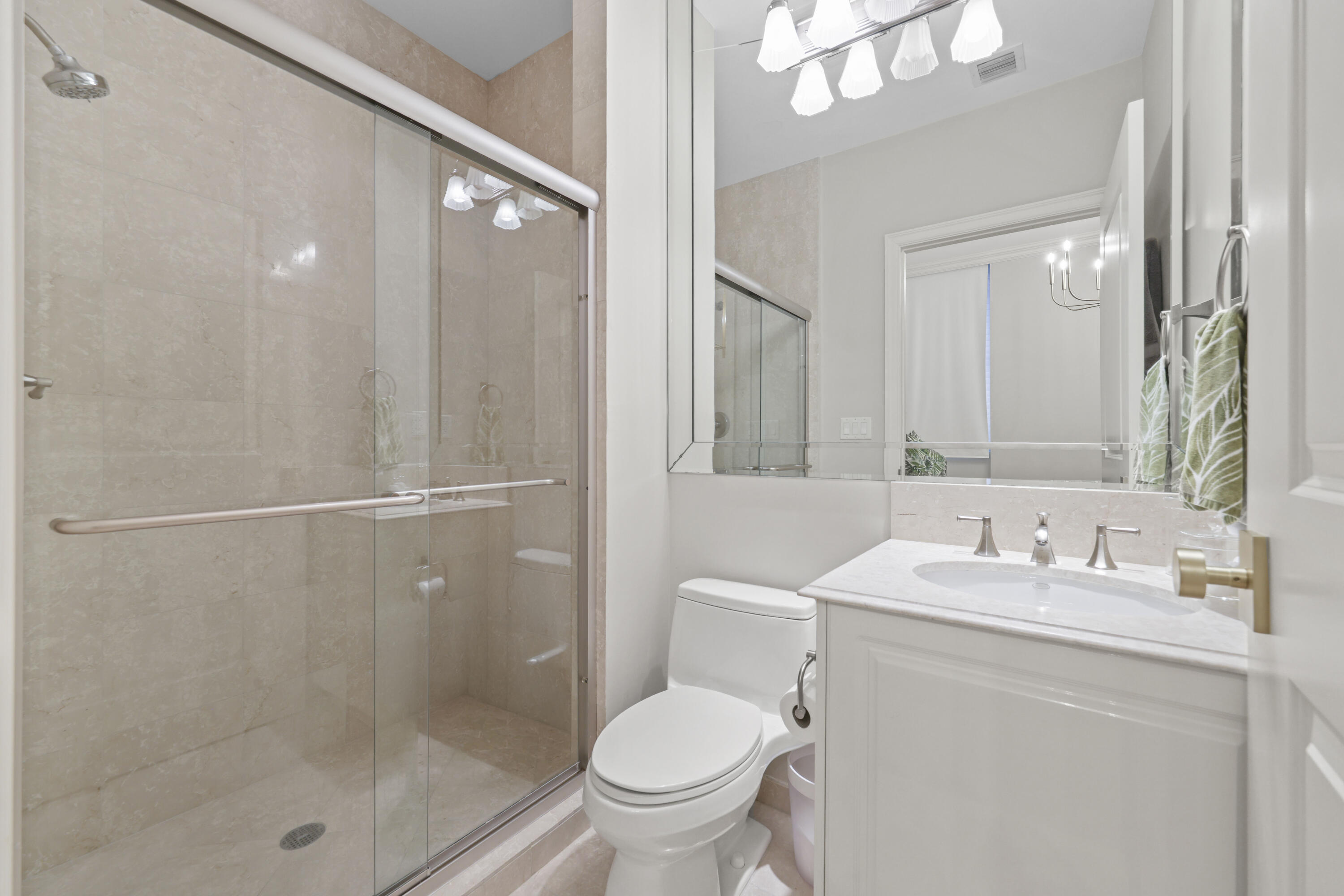 Bathroom with a glass-enclosed beige stone shower and white vanity.