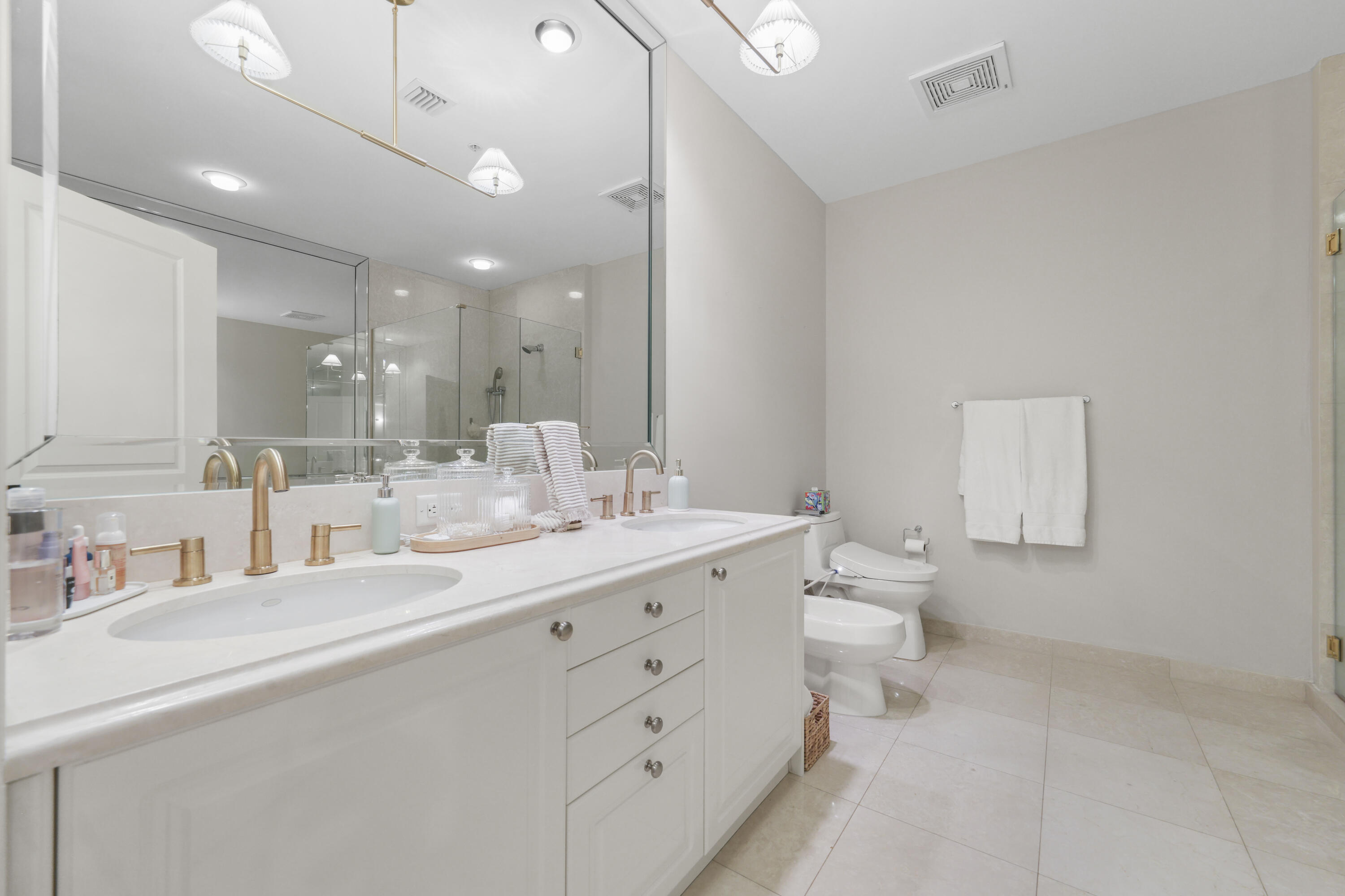 Bathroom with a long double-sink vanity, mirrored wall, and glass-enclosed shower.
