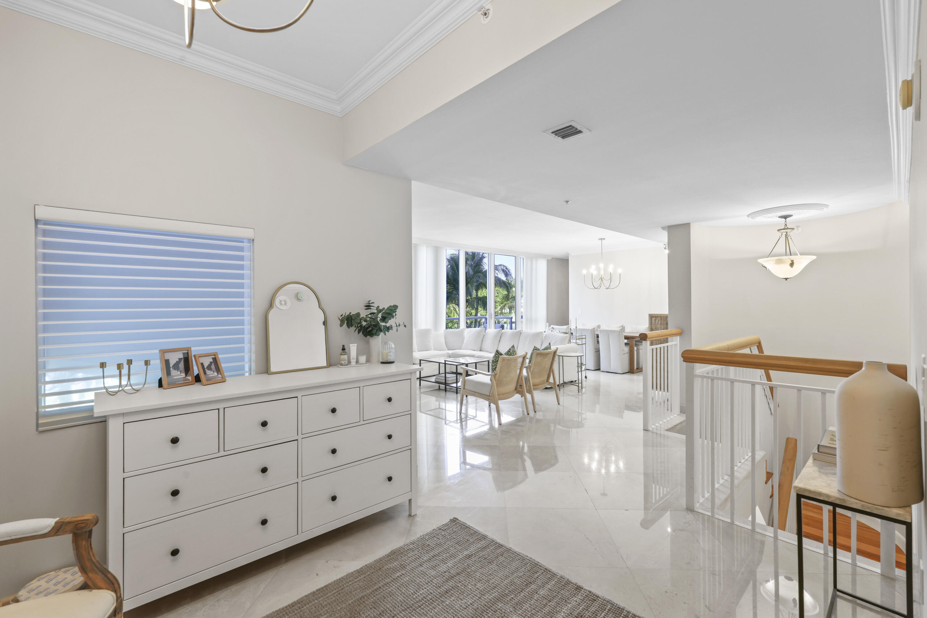 Open-plan living and dining area with polished tile floors and windows overlooking palm trees.