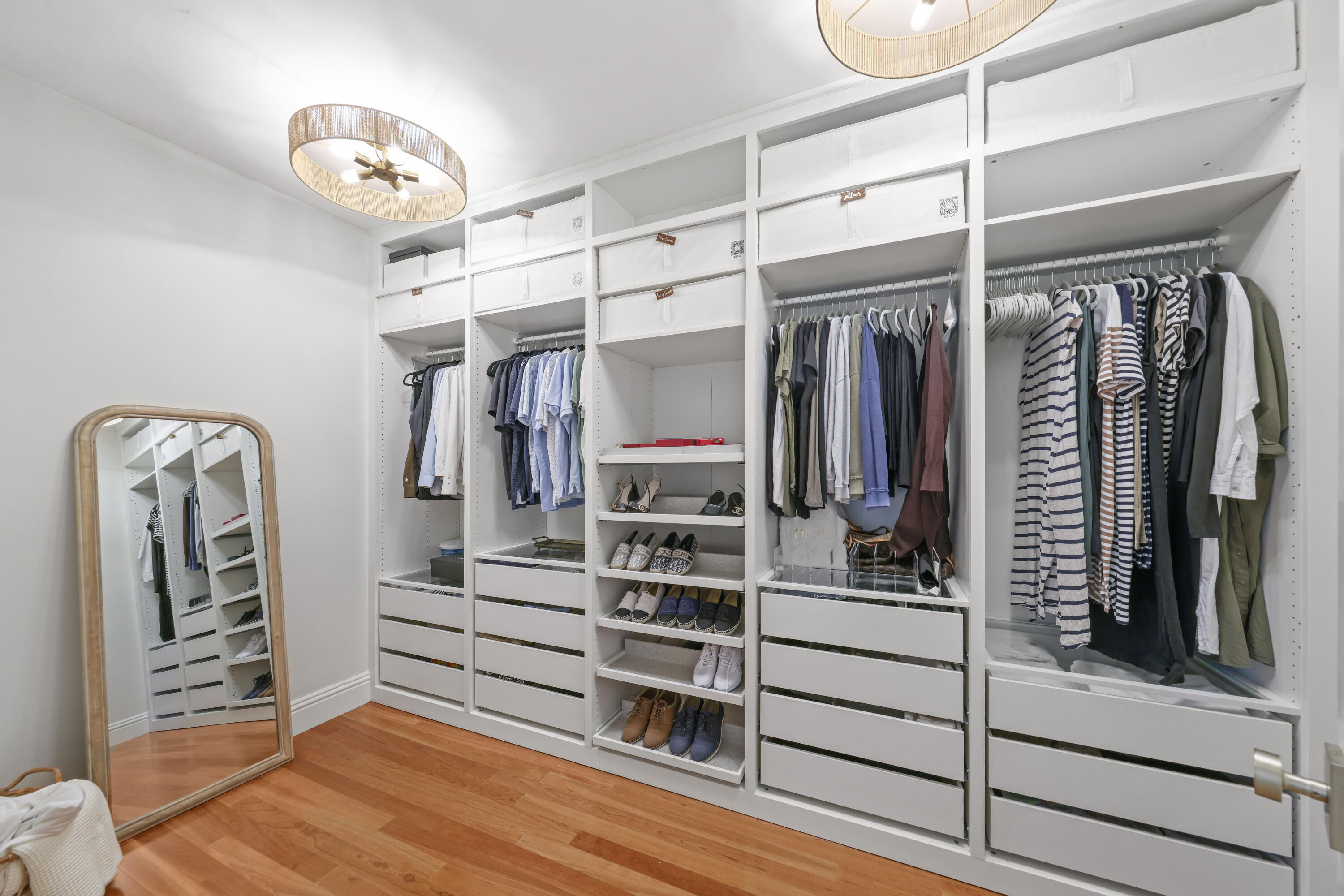 Walk-in closet with white built-ins, organized clothes and shoes, a full-length mirror, and wood flooring.