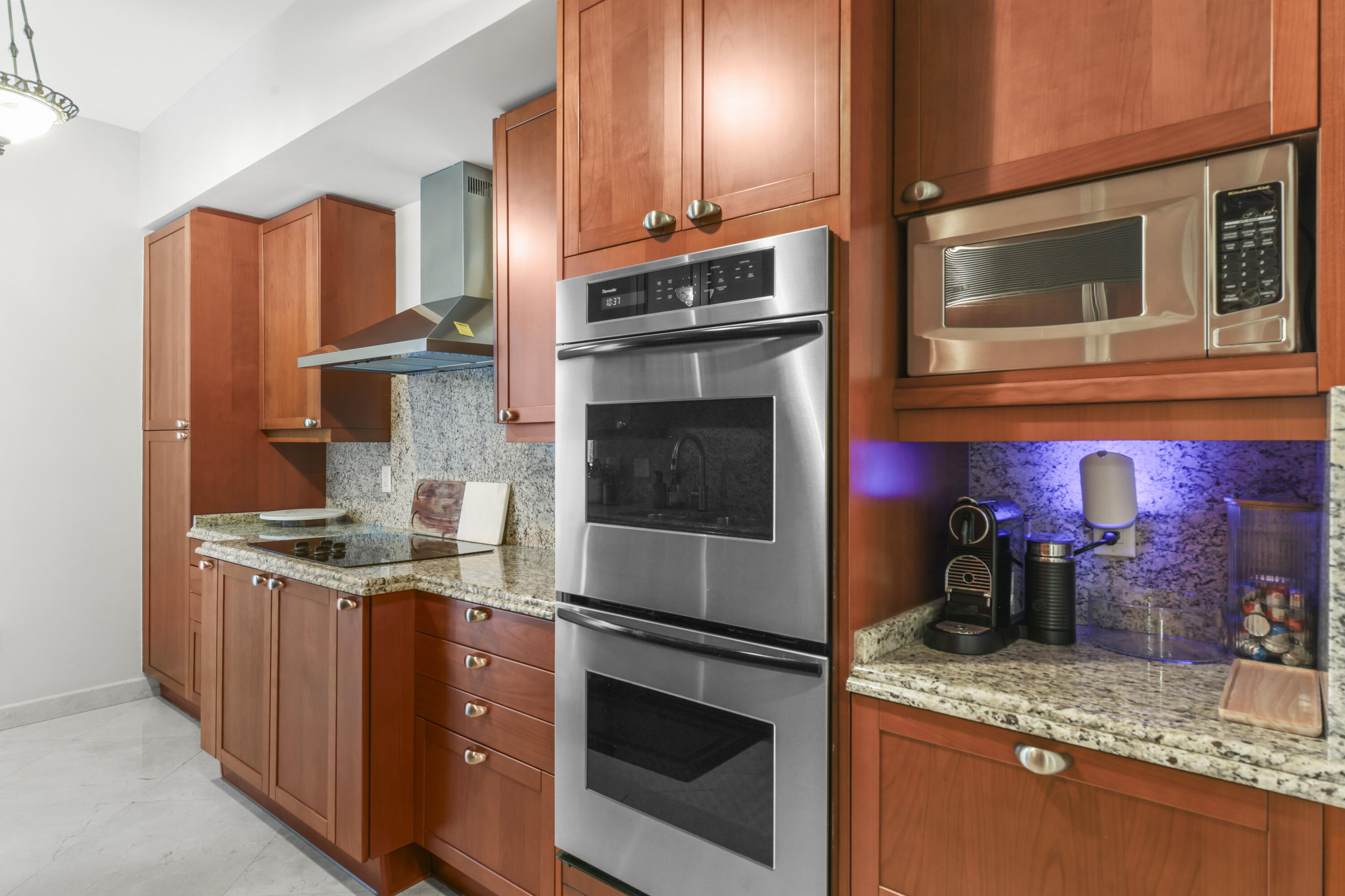 Kitchen with reddish wood cabinetry, granite counters, stainless double oven, and a coffee station with blue lighting.