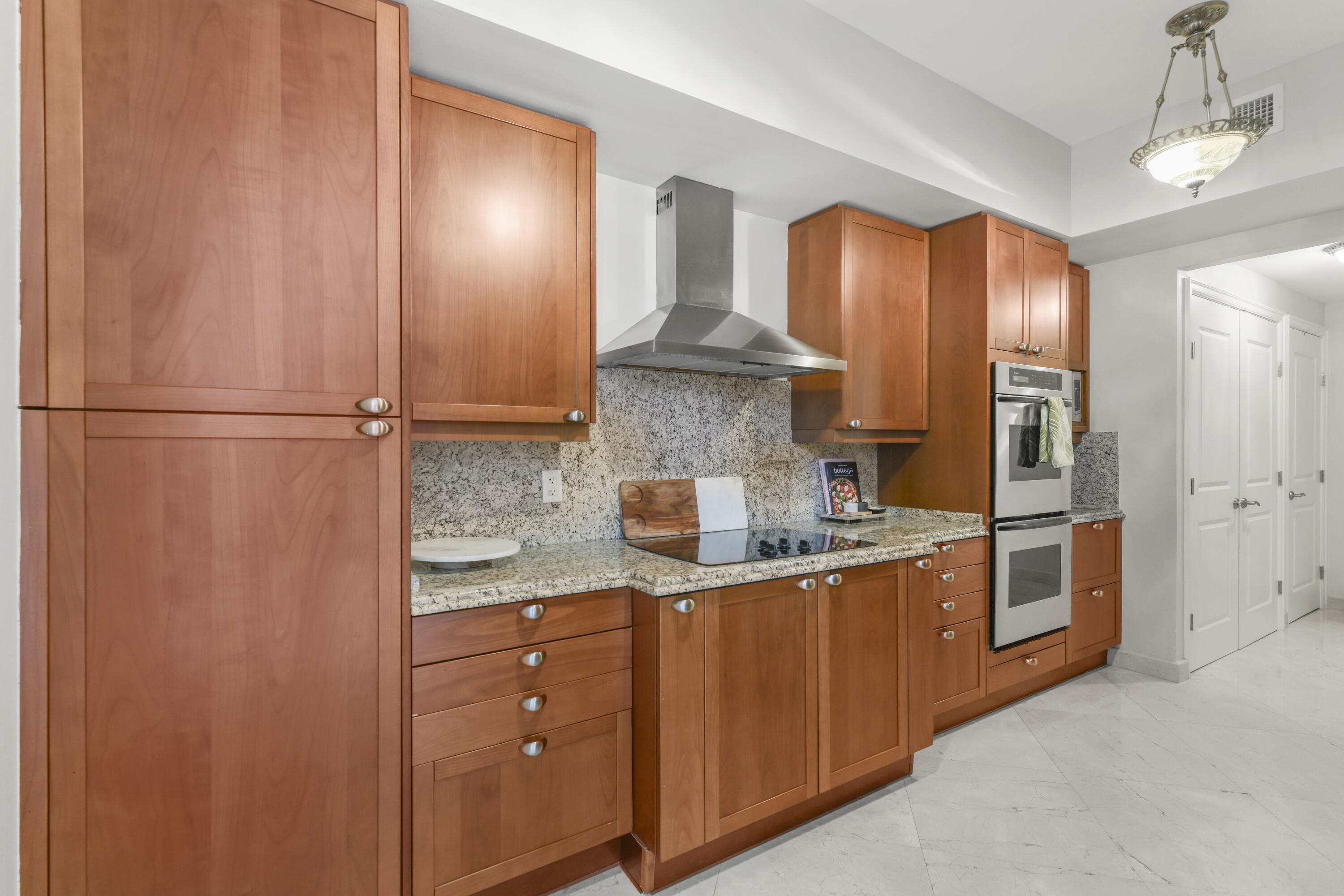 Kitchen with reddish-brown wood cabinets, granite counters, stainless steel hood, and double wall ovens.