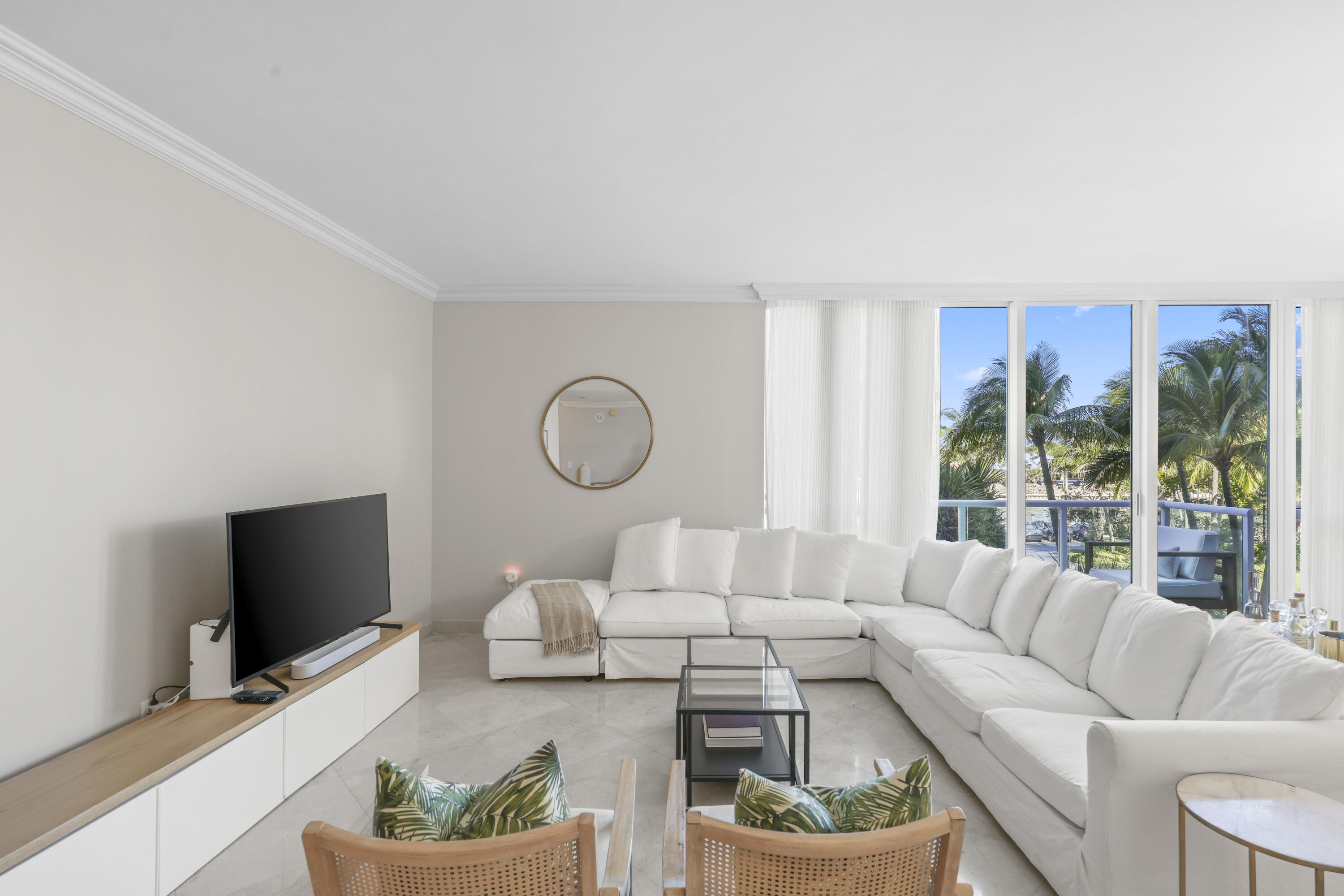 Living room with a white sectional sofa and palm trees visible through the windows.