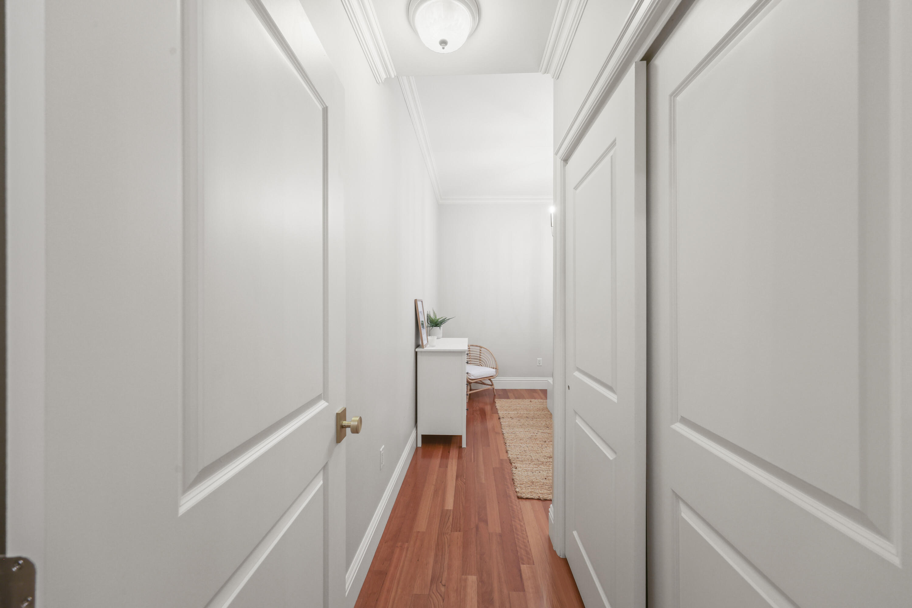 Bright hallway with white paneled doors, reddish hardwood floors, and a small furnished nook.