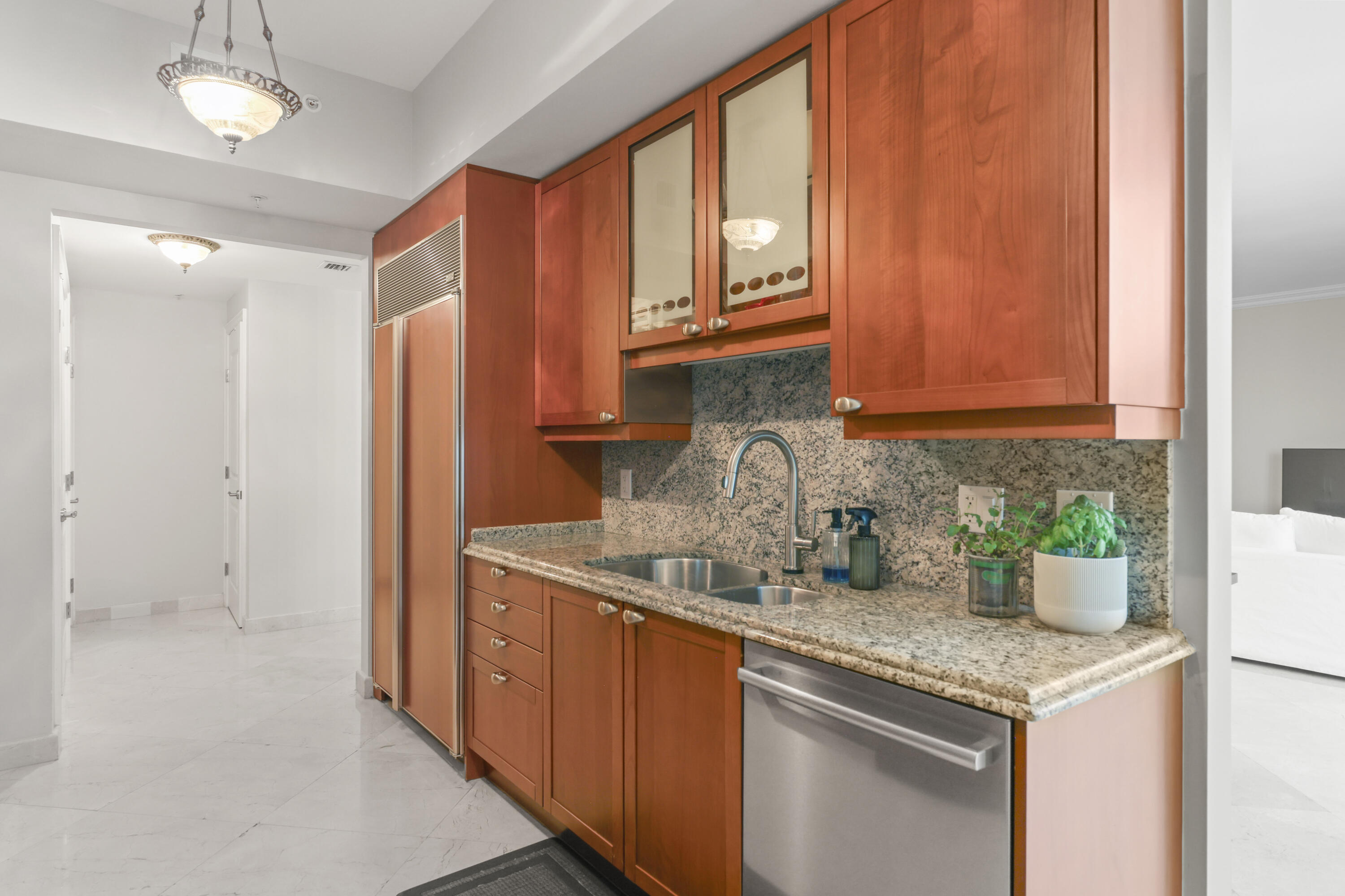 Condominium kitchen with reddish wood cabinets, granite counters, and a stainless steel dishwasher.