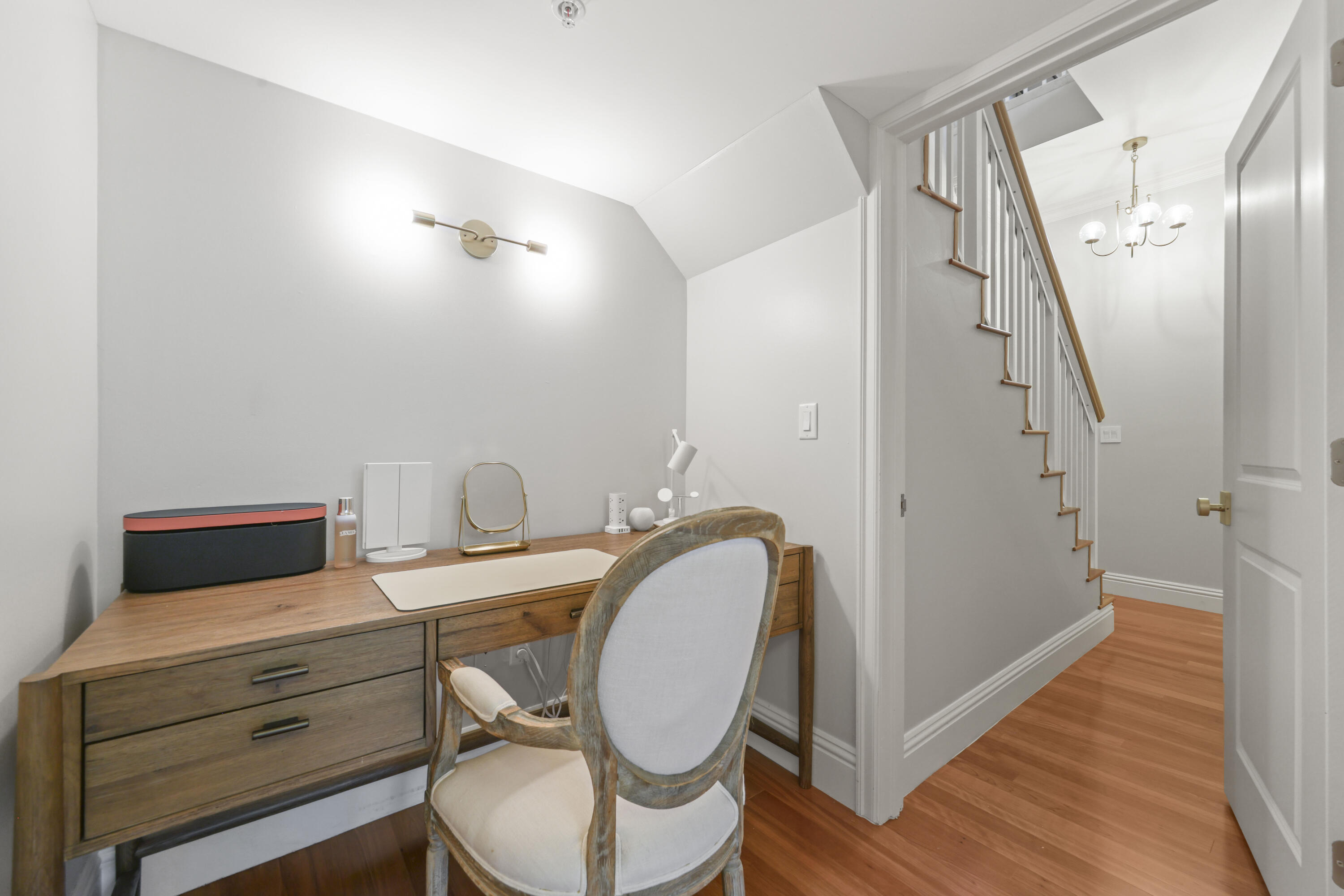 Home office with a wooden desk and upholstered chair beside an open staircase.