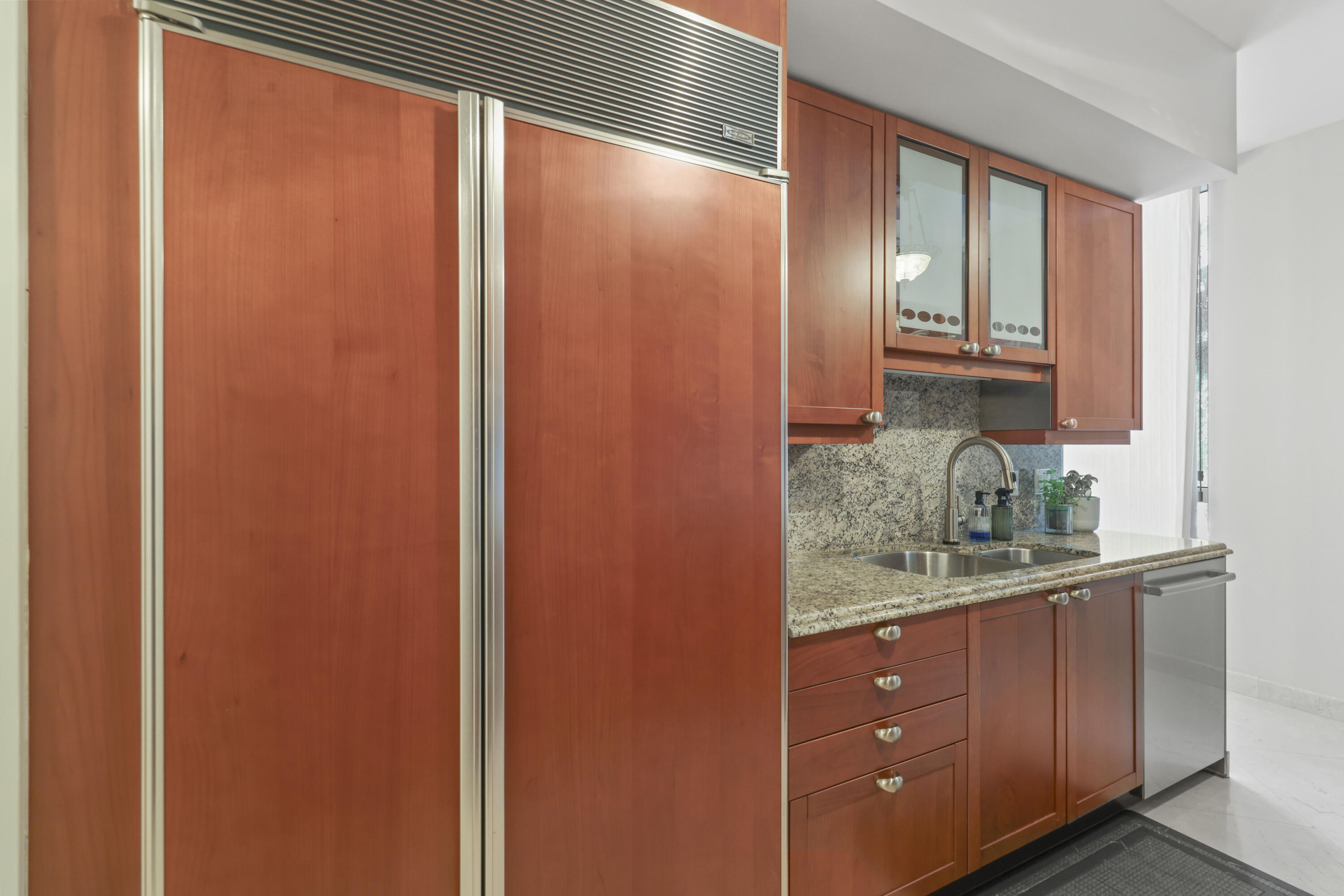Condominium kitchen with reddish wood cabinets, granite counters, a large refrigerator, and a double-basin sink.