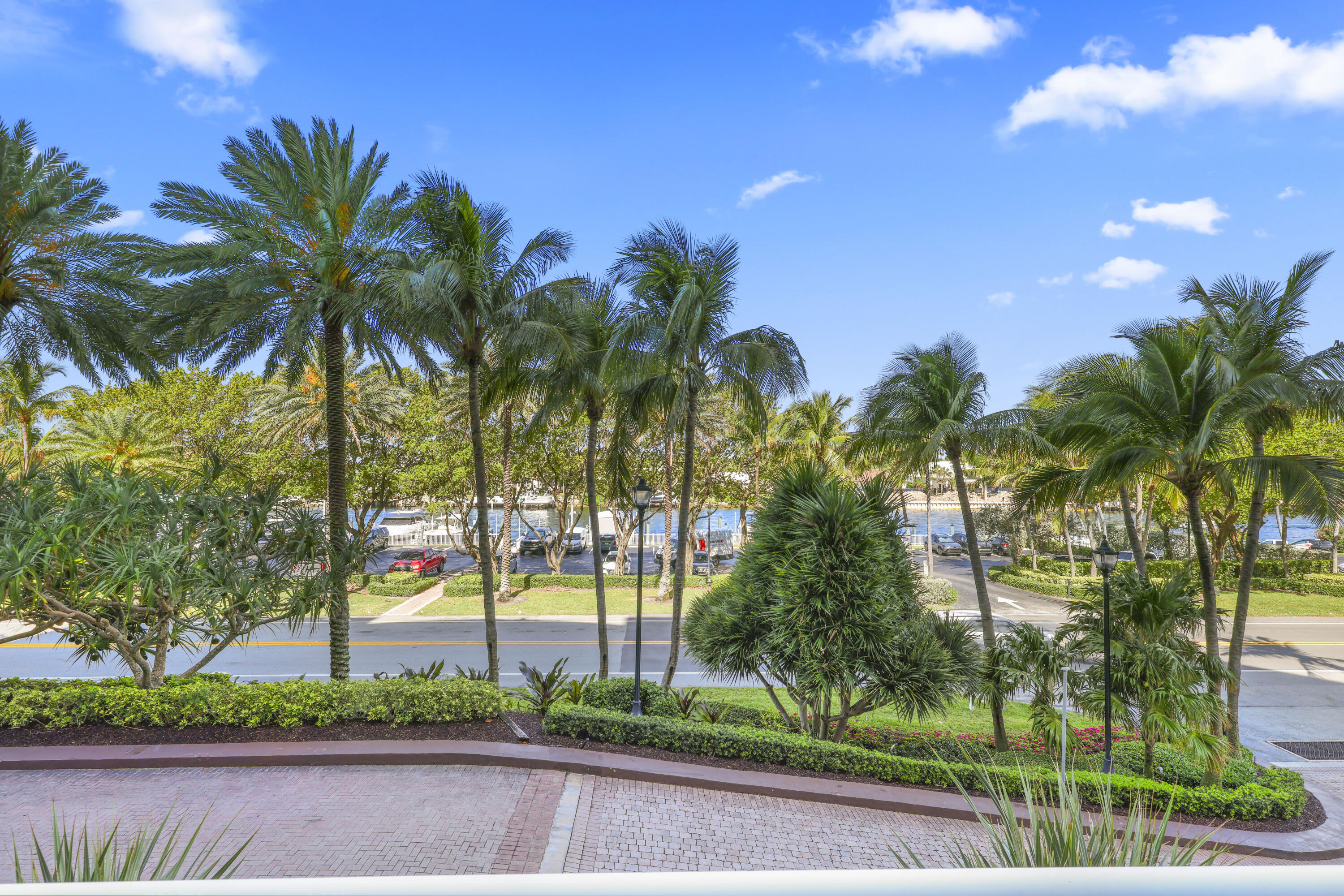 Palm-lined landscaped grounds overlook a road and boat-filled waterway.