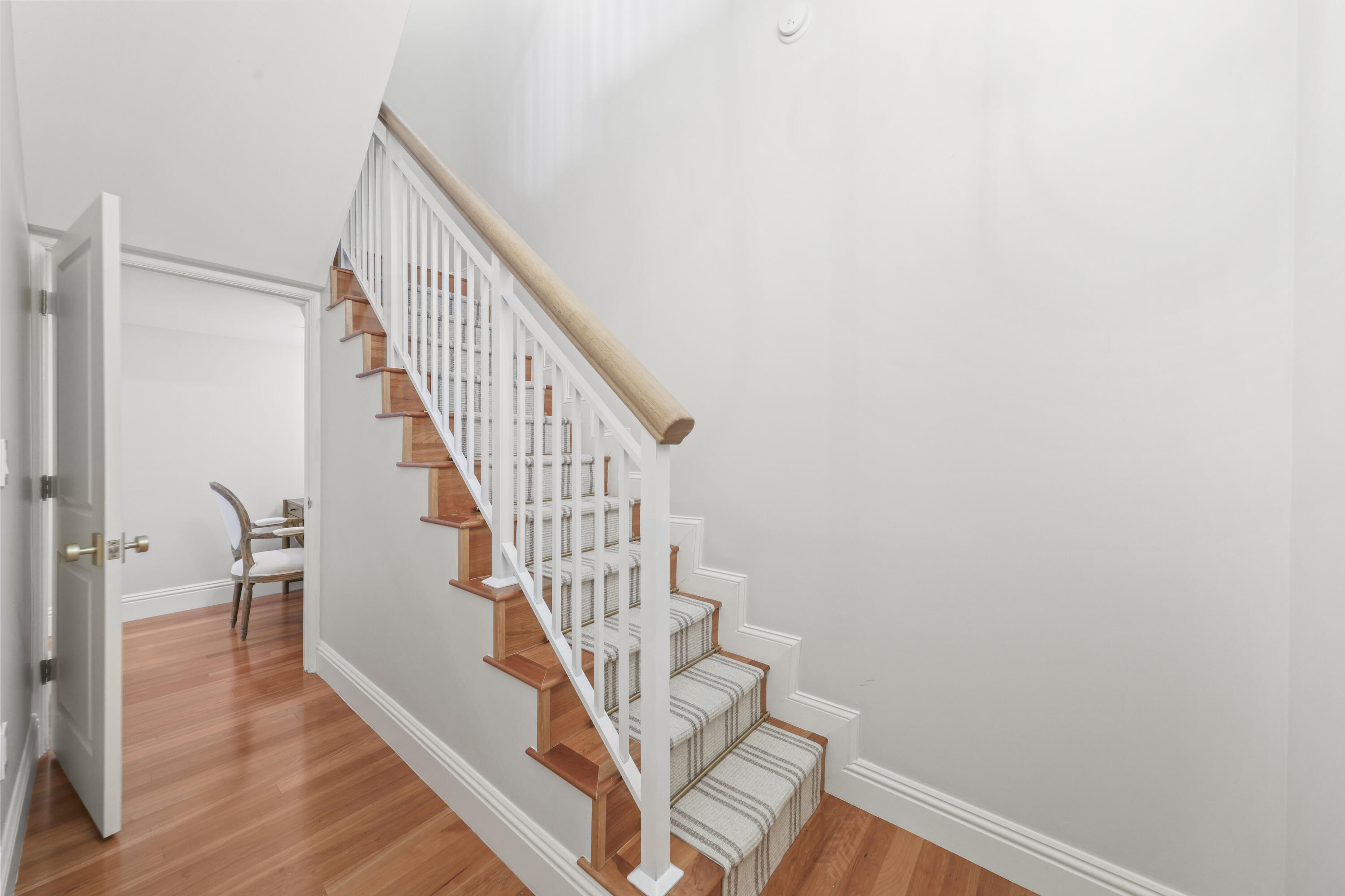 Hardwood staircase with a striped runner and white railing beside an open doorway.