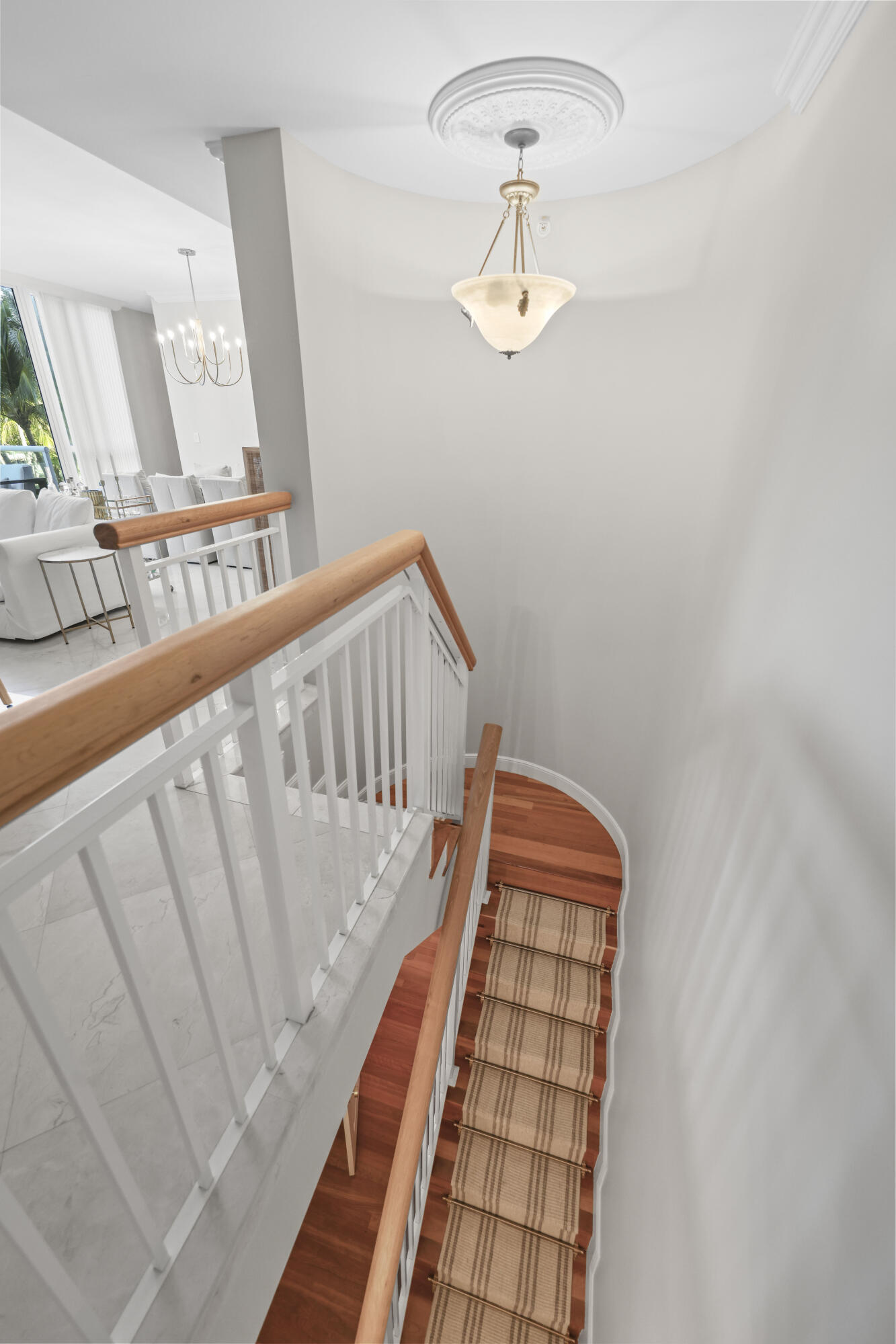Curved wood staircase with a patterned runner and white balusters, overlooking a bright living area.