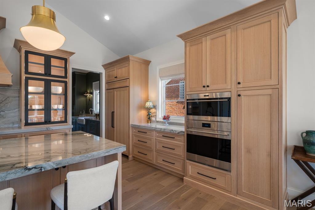 Kitchen with a marble island, light wood cabinetry, and built-in double ovens.