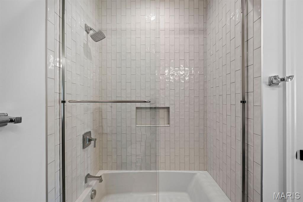 Tiled tub and shower with glass enclosure, recessed niche, and chrome fixtures.