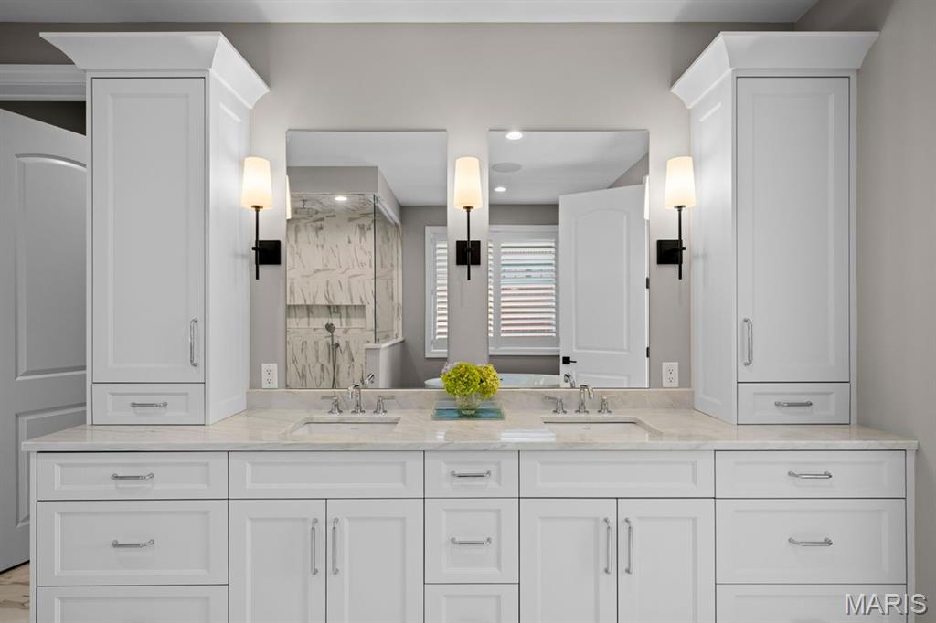 Bathroom vanity with double sinks, white cabinetry, marble countertop, and wall sconces.